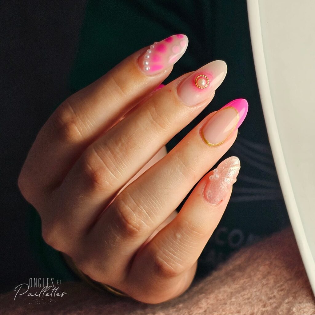 Ongles colorés. Des ongles nail art, l'index a des points roses avec des perles blanches, sur le majeur on observe un cercle doré et une perle à l'intérieur, l'auriculaire a aussi 3 petites perles et des motifs en relief.