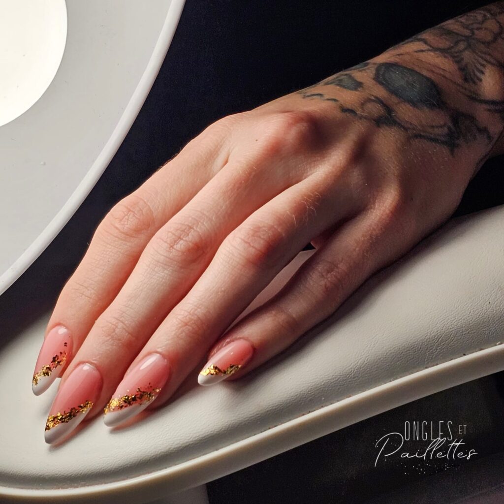 Ongles bicolores en forme d'amande. Les ongles sont roses et blancs, divisés par une ligne de feuilles d'or.