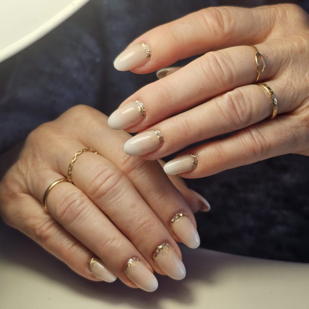 Manucure, pose de vernis de couleur sobre, nude, beige. Avec une touche de dorée pailletée à la place des cuticules.